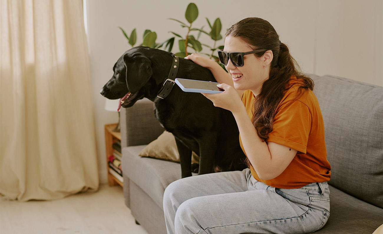 Una mujer ciega utiliza un smartphone sentada al lado de su perro.