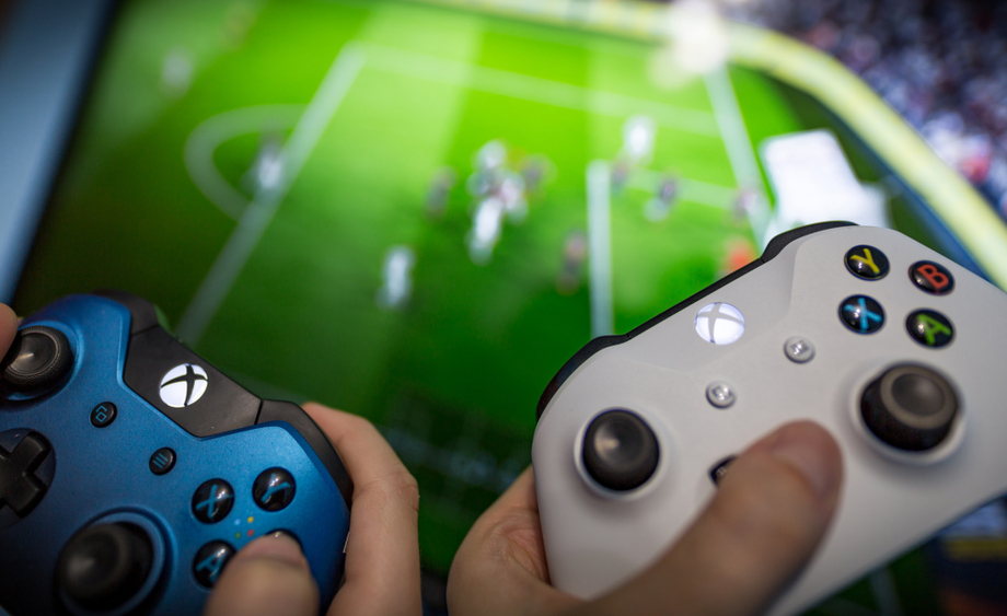 Dos j&oacute;venes sujetan sendos mandos de la Xbox One delante de un televisor